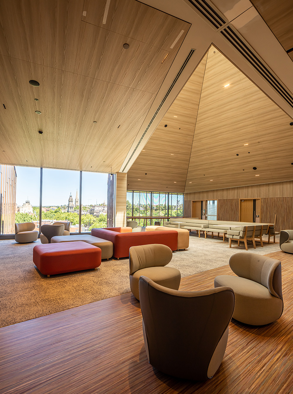 A large room with vaulted timber ceilings and comfortable chairs looks outside to the Bendigo skyline